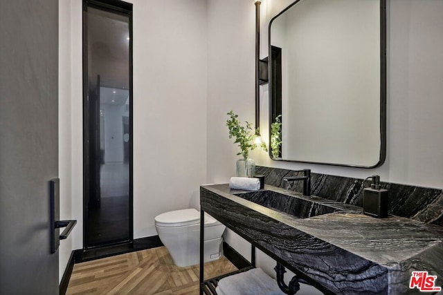 bathroom featuring toilet, parquet floors, and sink