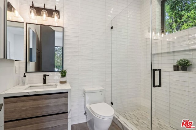 bathroom with tile walls, walk in shower, vanity, and toilet