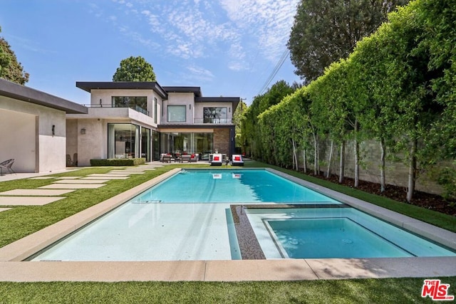 rear view of property with a balcony and a swimming pool with hot tub