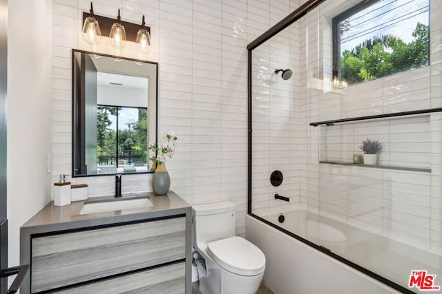 full bathroom with toilet, shower / bath combination with glass door, tile walls, and vanity