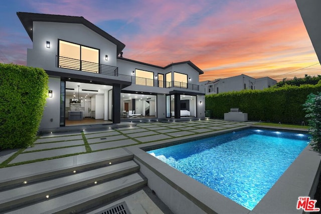 back house at dusk with a fenced in pool, a patio area, and a balcony