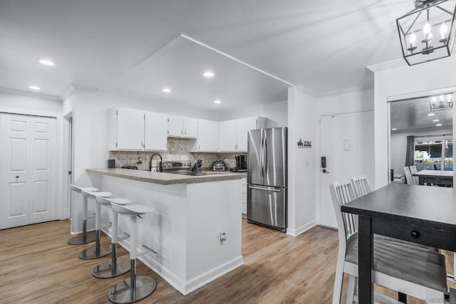 kitchen featuring backsplash, white cabinets, light hardwood / wood-style floors, kitchen peninsula, and stainless steel appliances