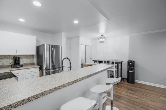 kitchen with white cabinetry, a breakfast bar area, stainless steel fridge, dark hardwood / wood-style flooring, and backsplash