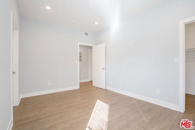 unfurnished bedroom featuring electric panel, a walk in closet, light wood-type flooring, and a closet