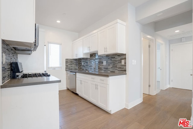 kitchen with stainless steel dishwasher, backsplash, white cabinets, stove, and sink