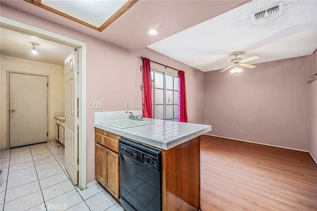 kitchen featuring a textured ceiling, light tile patterned floors, ceiling fan, black dishwasher, and sink