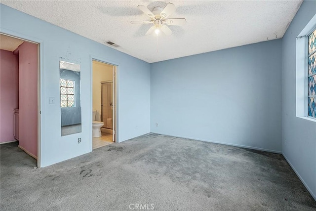 unfurnished bedroom featuring ensuite bath, a textured ceiling, carpet floors, and ceiling fan