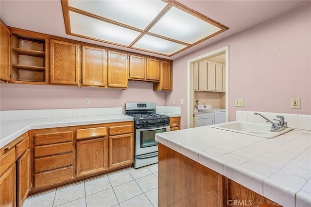 kitchen with sink, stainless steel gas stove, tile counters, and washing machine and clothes dryer