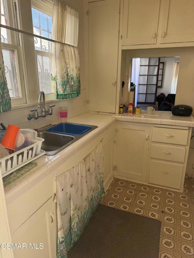 kitchen featuring white cabinets, tile counters, tasteful backsplash, and sink