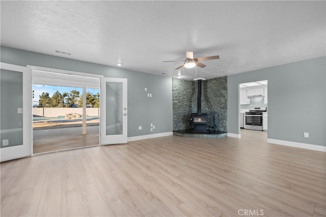 unfurnished living room with a textured ceiling, a wood stove, french doors, ceiling fan, and light wood-type flooring