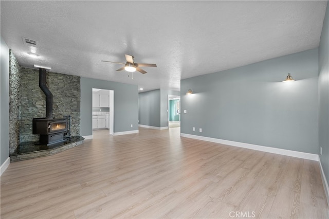 unfurnished living room featuring a textured ceiling, light wood-type flooring, and a wood stove