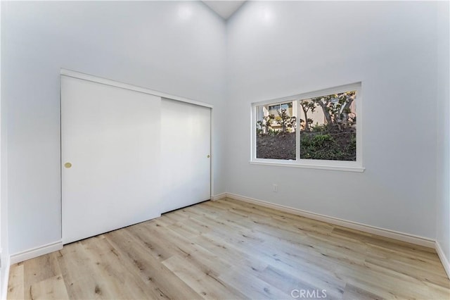 unfurnished bedroom with a high ceiling, a closet, and light hardwood / wood-style flooring