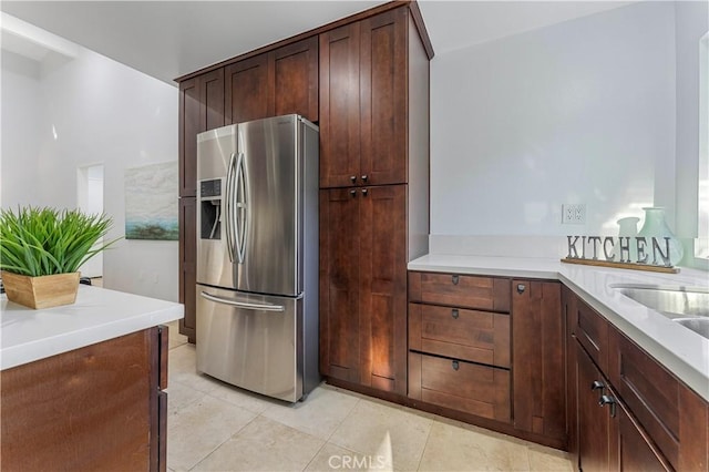 kitchen with stainless steel refrigerator with ice dispenser, sink, light tile patterned floors, and dark brown cabinetry