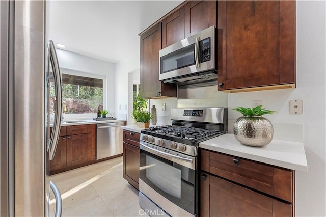 kitchen with sink, stainless steel appliances, light tile patterned flooring, and dark brown cabinetry