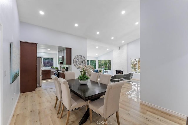 dining area with light hardwood / wood-style flooring, high vaulted ceiling, and a fireplace