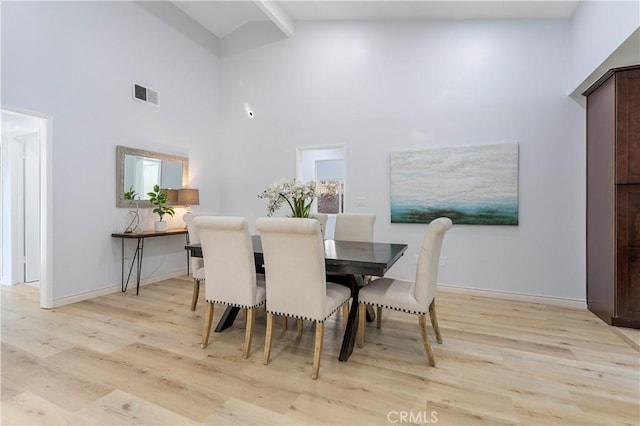 dining space featuring high vaulted ceiling, light hardwood / wood-style floors, and beam ceiling