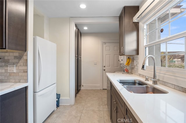 kitchen featuring sink, backsplash, white fridge, and dark brown cabinetry