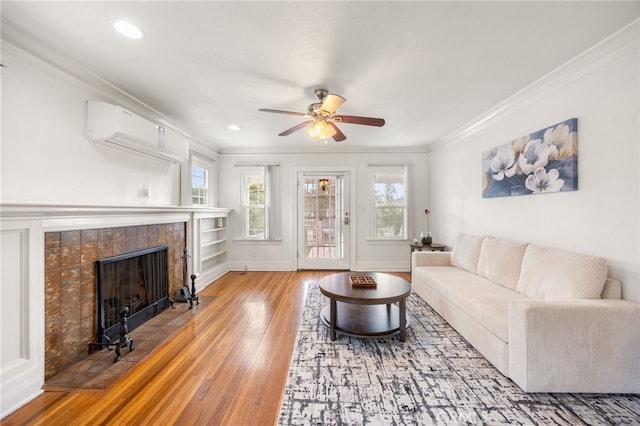 living room with a fireplace, an AC wall unit, hardwood / wood-style floors, ceiling fan, and crown molding