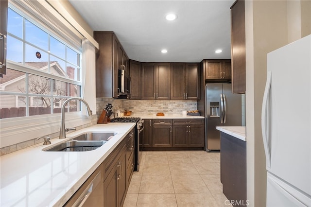 kitchen with appliances with stainless steel finishes, light tile patterned floors, sink, dark brown cabinets, and backsplash