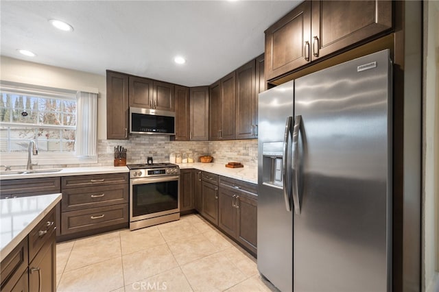 kitchen featuring stainless steel appliances, light tile patterned floors, sink, dark brown cabinets, and tasteful backsplash