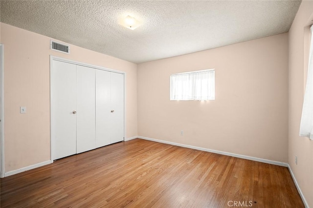 unfurnished bedroom featuring a textured ceiling, light wood-type flooring, and a closet