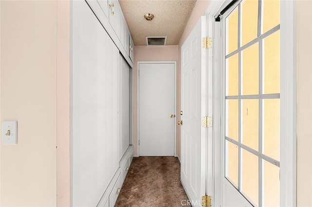 corridor featuring a textured ceiling and dark colored carpet