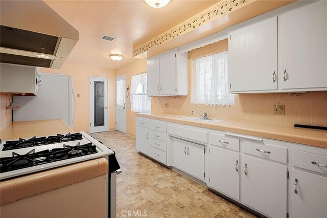 kitchen featuring white appliances, tile counters, exhaust hood, white cabinets, and sink