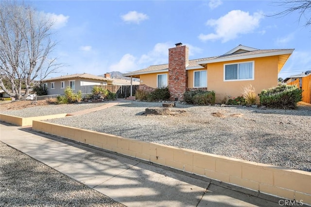 ranch-style home featuring fence, a chimney, and stucco siding