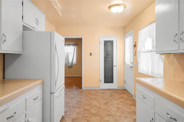 kitchen with white cabinetry, white fridge, tasteful backsplash, and tile counters