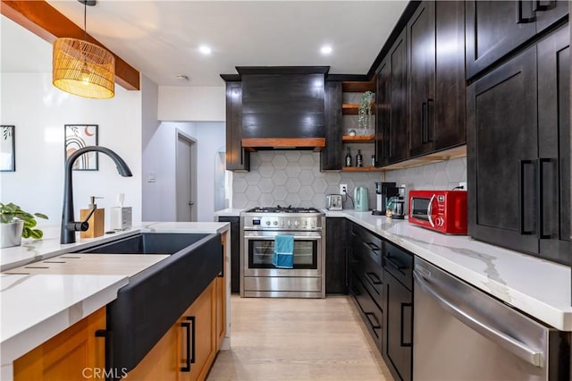 kitchen with wall chimney range hood, stainless steel appliances, tasteful backsplash, hanging light fixtures, and light stone counters