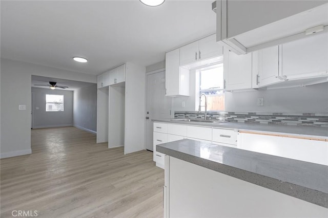 kitchen with light wood-type flooring, ceiling fan, sink, white cabinetry, and tasteful backsplash