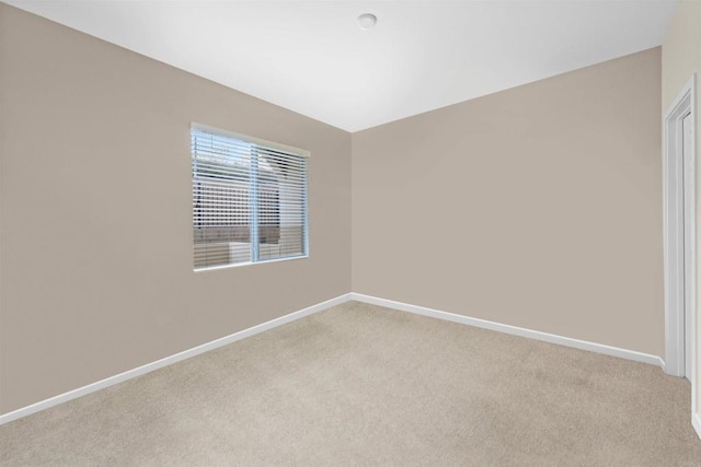 spare room featuring light colored carpet and baseboards