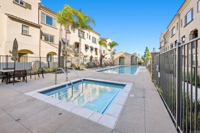 pool featuring a community hot tub, a patio area, fence, and a residential view