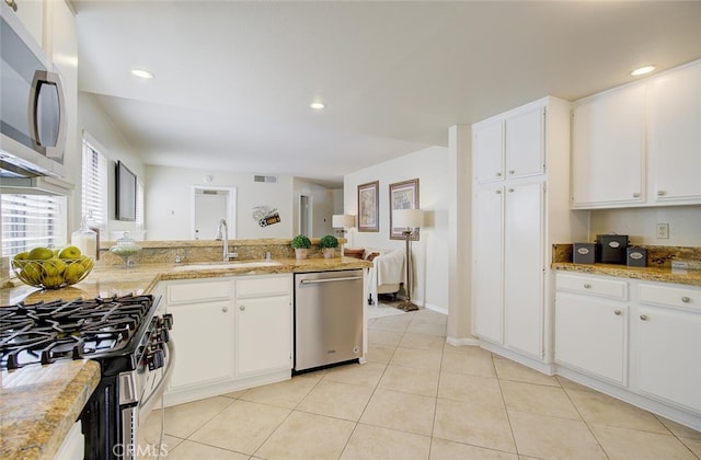 kitchen with appliances with stainless steel finishes, white cabinets, light stone counters, and sink