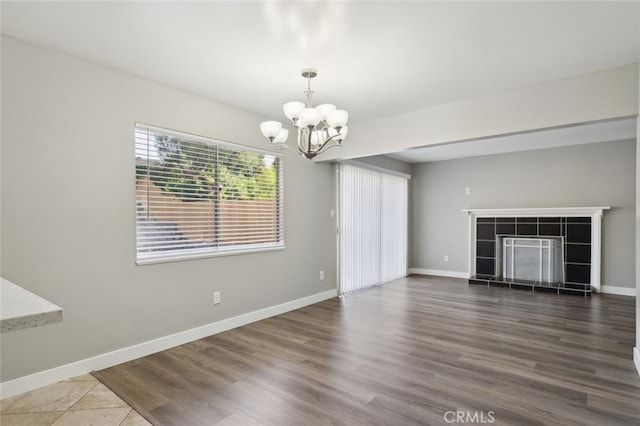 unfurnished living room with hardwood / wood-style flooring, a tiled fireplace, and a notable chandelier