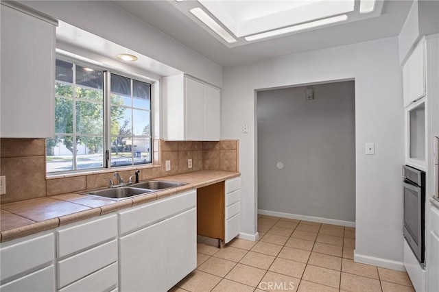 kitchen featuring light tile patterned flooring, white cabinetry, tile counters, oven, and backsplash