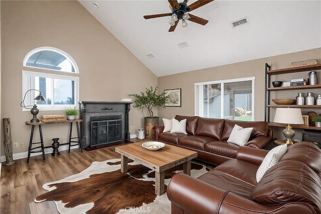 living room featuring a ceiling fan, wood finished floors, visible vents, high vaulted ceiling, and a fireplace