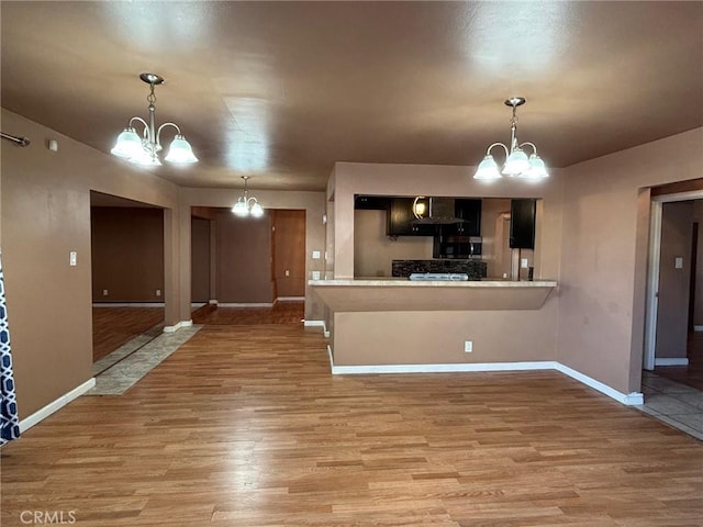 kitchen featuring hardwood / wood-style floors, kitchen peninsula, a notable chandelier, a kitchen bar, and wall chimney range hood