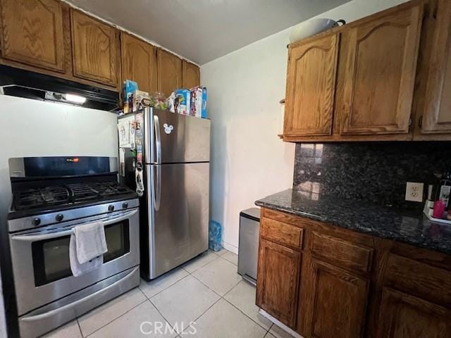 kitchen with stainless steel appliances, dark stone countertops, light tile patterned flooring, and tasteful backsplash