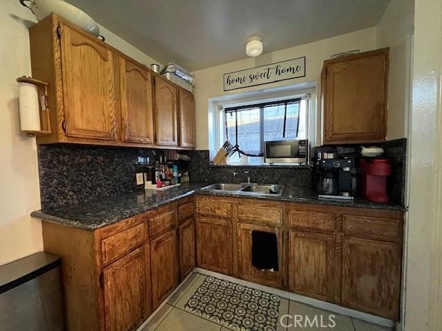 kitchen featuring dark stone countertops, light tile patterned floors, tasteful backsplash, and sink