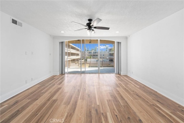 unfurnished room with ceiling fan, a wall of windows, a textured ceiling, and hardwood / wood-style flooring