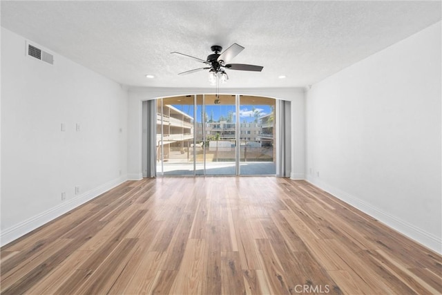 unfurnished room featuring a textured ceiling, wood finished floors, visible vents, and a ceiling fan