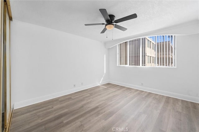 unfurnished room featuring a textured ceiling, wood finished floors, a ceiling fan, and baseboards