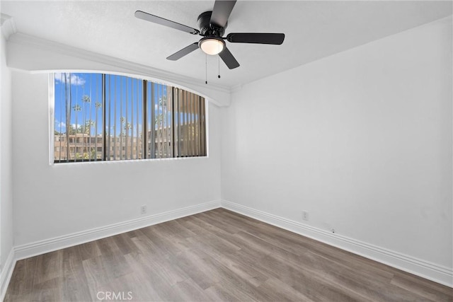 empty room featuring a ceiling fan, baseboards, wood finished floors, and ornamental molding