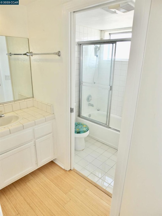 full bathroom featuring hardwood / wood-style floors, enclosed tub / shower combo, toilet, and vanity