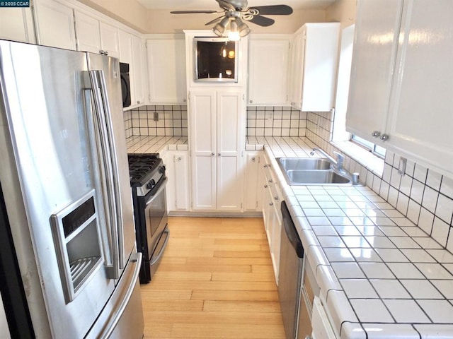 kitchen featuring tile countertops, stainless steel appliances, tasteful backsplash, white cabinetry, and sink