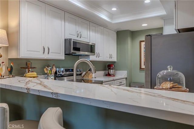 kitchen with a raised ceiling, stainless steel appliances, crown molding, light stone counters, and white cabinetry