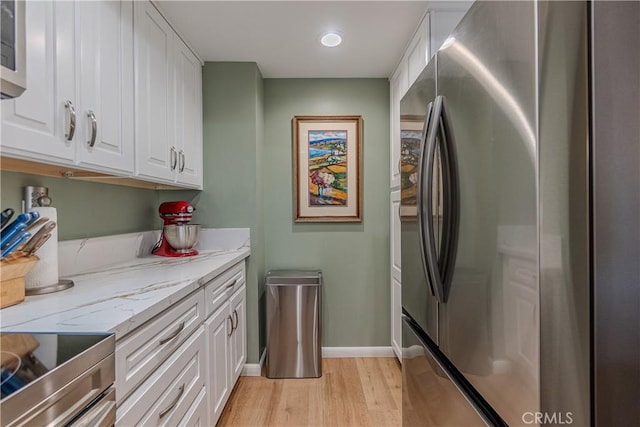 kitchen with light hardwood / wood-style floors, stainless steel fridge, light stone counters, range with electric stovetop, and white cabinetry