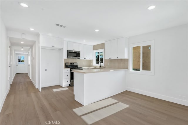 kitchen with light hardwood / wood-style floors, stainless steel appliances, kitchen peninsula, white cabinetry, and backsplash