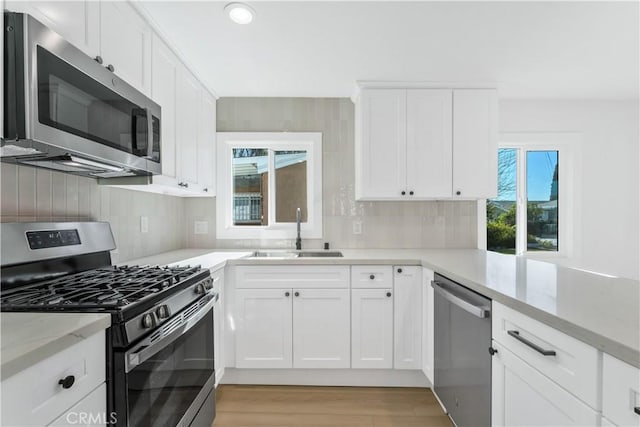 kitchen featuring sink, white cabinets, light stone counters, light hardwood / wood-style floors, and appliances with stainless steel finishes